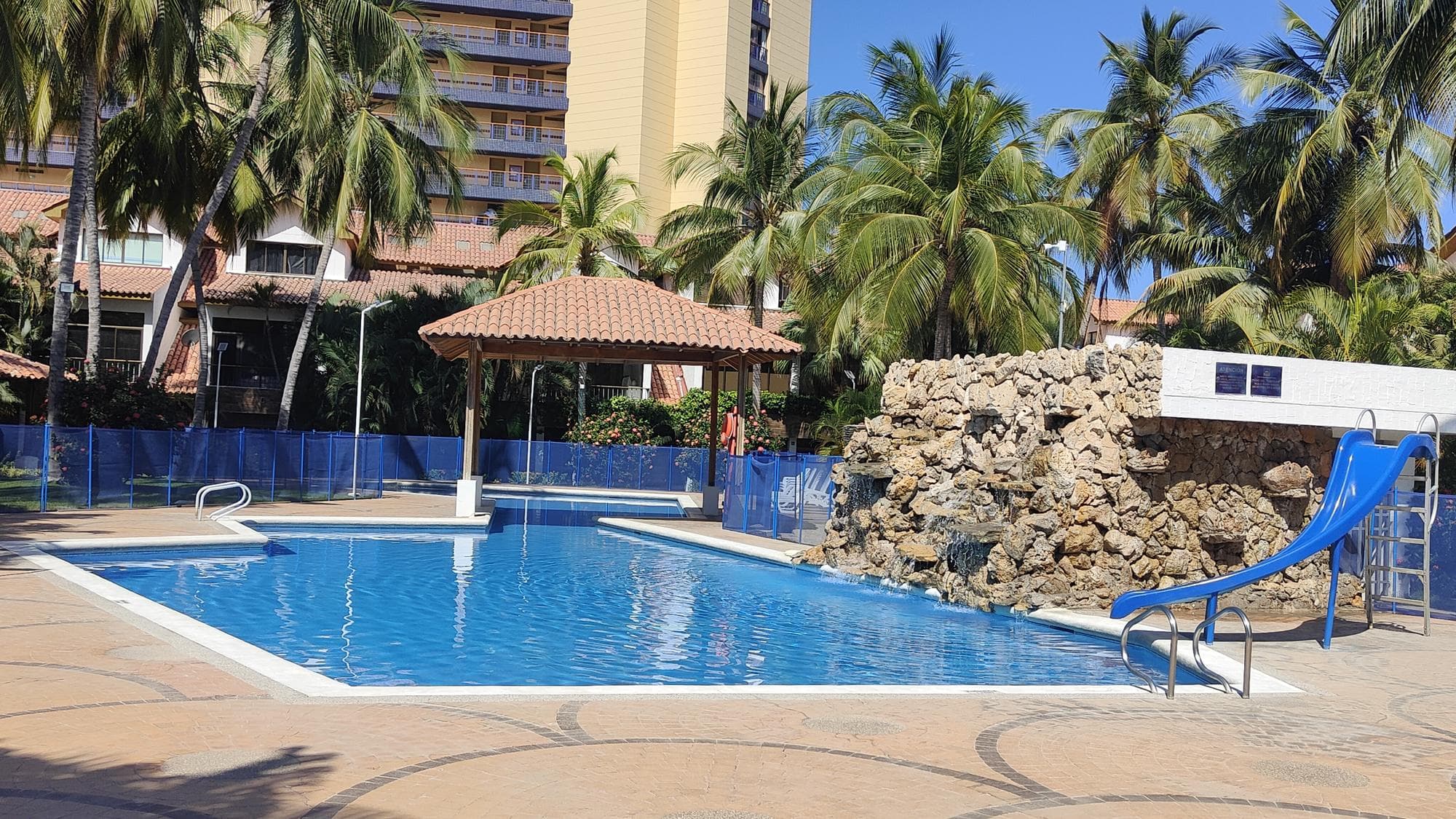 La piscina con lo scivolo blu, la cascata di pietra e il chiosco al centro